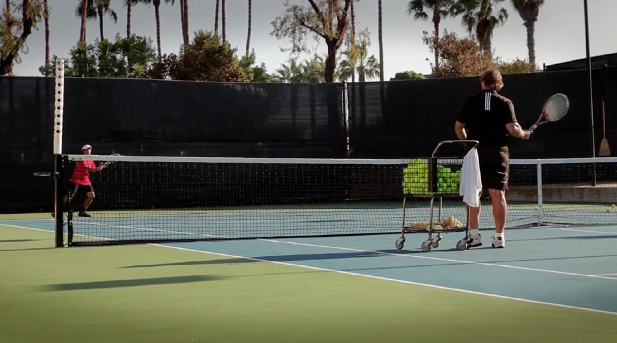 Mike coaching a rally across a palm-tree tennis court